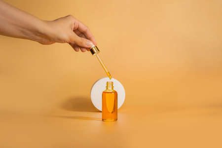 Dropper glass Bottle Mock-Up next to geometric shapes. Oily drop falls from cosmetic pipette on yellow background. Cosmetology and beauty concept.の写真素材