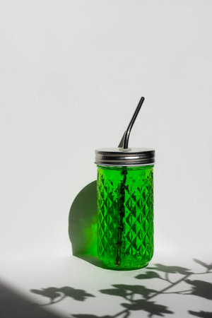 Transparent glass of with green lemonade with reusable metal eco straw in sunlight with shadow.の写真素材