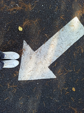 White arrow on the asphalt road in the autumn. top view.