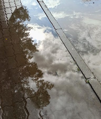 Reflection of clouds in a puddle of water on the sidewalkの写真素材