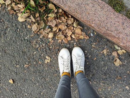 Selfie of female feet in white sneakers standing on the asphalt.の写真素材