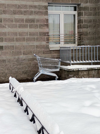 Shopping cart covered with snow in front of a residential building.の写真素材