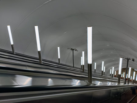 Interior of a subway station with escalators and white lamps.