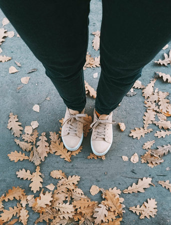 Female legs in jeans and sneakers on the background of autumn leaves.