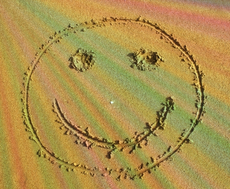 smiley face in the sand with multi-colored rays of the sunの写真素材
