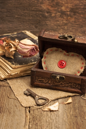 Valentine decorations with chest with hearts, key, dry rose, old book on wooden background (toning, grunge).の写真素材