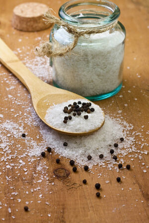 wooden spoon with sea salt and black pepper,  glass jar on a wooden backgroundの写真素材