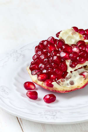 pomegranate seeds,  piece of pomegranate on  white plate on light background (selective focus)の写真素材