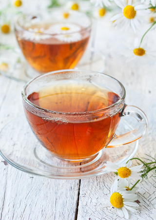 Chamomile tea in glass cups, a bouquet of camomiles on a white wooden backgroundの写真素材