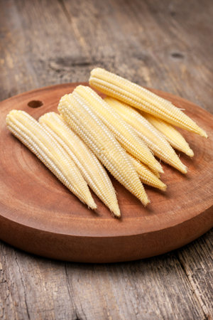 pile of small young corn cobs on the wooden background  close up