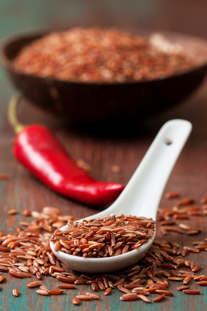 The spoon with red rice, chili peppers, bowl with rice on a wooden background. Selective focusの写真素材