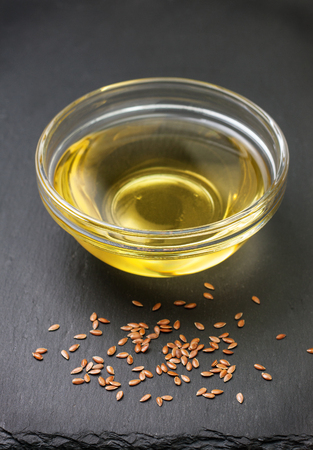 linseed oil in a glass bowl, flax seeds on black stone backgroundの写真素材