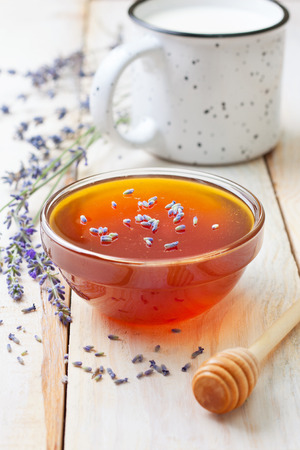 Fresh honey in a glass bowl and lavender, cup of milk on a wooden backgroundの写真素材
