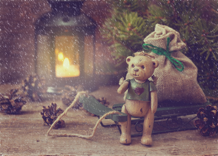 Christmas composition  with the bear, sled with bag of gifts, candle lantern, Christmas tree on the old wooden background. (Toning, snow effect)の写真素材