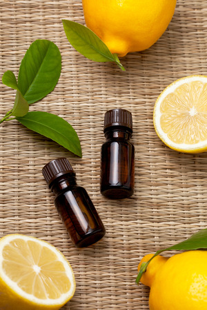 two bottles of lemon essential oil, fresh lemon on a straw background (selective focus)の写真素材