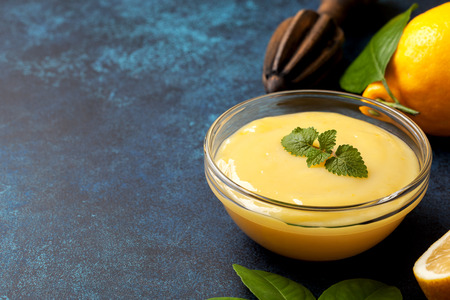 lemon curd in a glass bowl, fresh lemons, juicer on a blue backgroundの写真素材