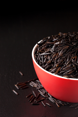 Black wild rice in a red bowl on a black backgroundの写真素材