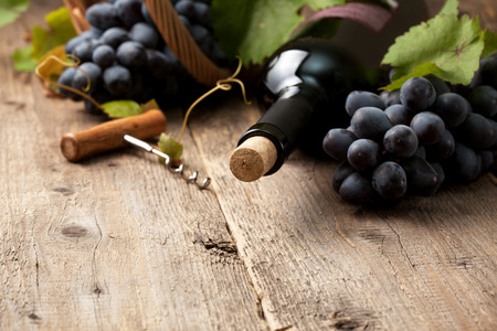 bottle of wine and grapes in basket on old wooden backgroundの写真素材