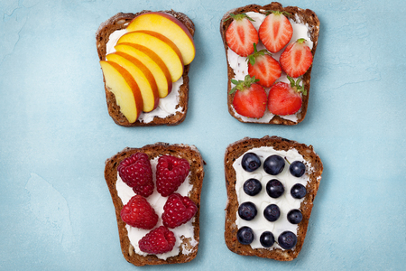 Diet breakfast. Toasts with cream cheese and fresh berries and fruits: banana, raspberry, blueberry, strawberry, peach. Top viewの写真素材