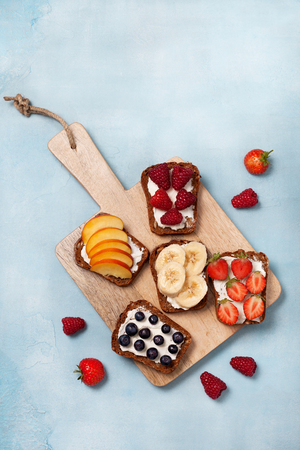 Diet breakfast. Toasts with cream cheese and fresh berries and fruits: banana, raspberry, blueberry, strawberry, peach. Top viewの写真素材