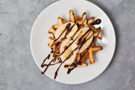 Waffles with banana and chocolate sauce on a gray concrete background. view from aboveの写真素材