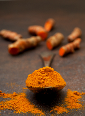 turmeric powder in an old vintage spoon, turmeric roots on a dark backgroundの写真素材