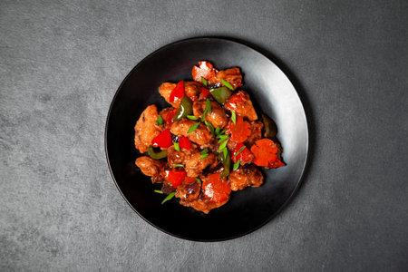 Manchurian chicken with vegetables on a black plate. view from above