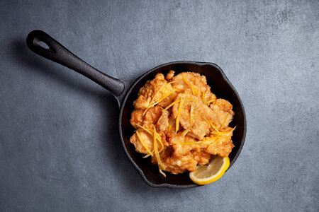 chicken fried with lemon sauce in a frying pan on a black backgroundの写真素材