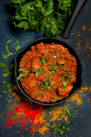 Chicken tikka masala in a cast-iron pan, vegetables on a blue background. view from above