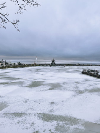 A beautifully serene winter scene showcasing a picturesque frozen lake and a charming lighthouse beneath cloudy skies.の写真素材