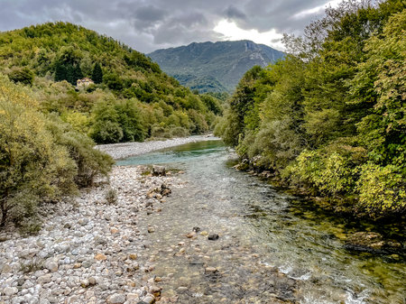 A peaceful and tranquil river gracefully meanders through lush and vibrant greenery beneath a cloudy skyの写真素材