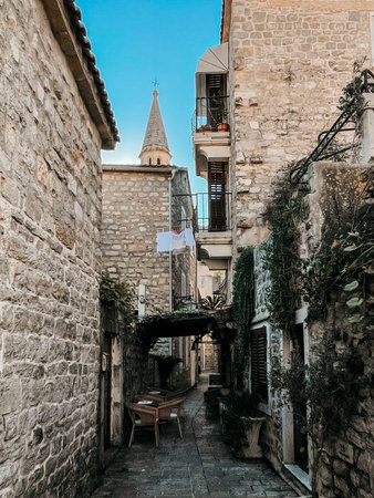 quiet alleyway table under laundry lines with woven chairs and small canopy, stone walls and narrow corridor create cozy dining nook, soft lantern light and muted skyの写真素材