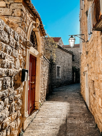 sunlit winding cobblestone lane with warm stone walls and wooden doors, narrow uphill path curving toward distant spire, terracotta tones and soft glow evoke solitude,の写真素材