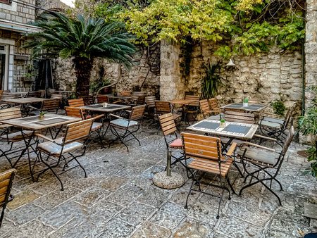empty mediterranean stone courtyard cafe with wooden folding chairs, bistro tables set with glasses and smallの写真素材