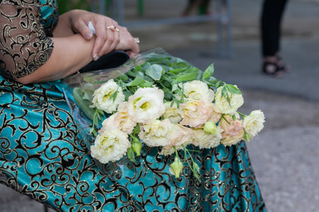 A mature woman with a bouquet of carnations in her hands sits on a chair in a turquoise dress. Close-up bouquetの写真素材