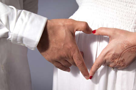 Pregnant woman and man close-up. Hands holding on the belly of a woman. Fingers in the shape of a heartの写真素材