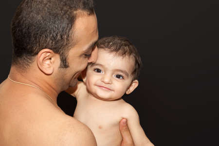 The father holds his son in his arms. Studio portrait over isolated dark background.の写真素材