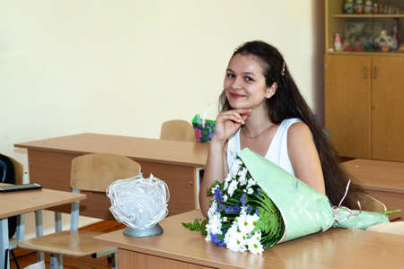 A schoolgirl girl sits at a desk in a classroom on September 1st. Indoor portrait.の写真素材