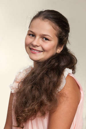 Portrait of a teenage girl in a pink dress and long wavy light brown hair. Studio photo .の写真素材