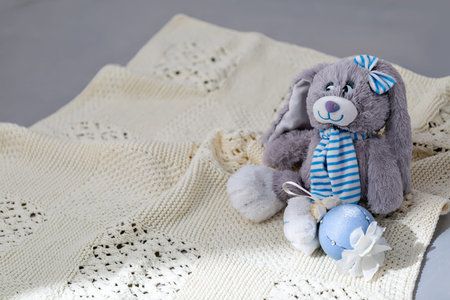 An ivory knitted baby blanket with a pronounced texture of the pattern and a soft toy on it. Window...