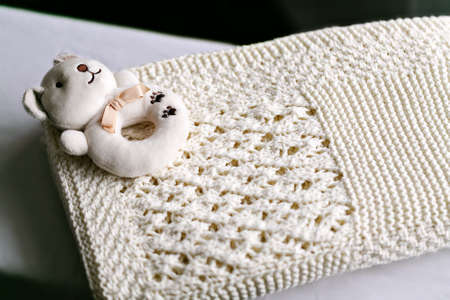 An ivory knitted baby blanket with a pronounced texture of the pattern and a soft toy on it. Window light.の写真素材