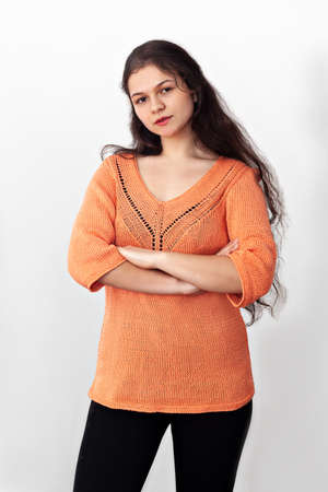 Portrait of a young girl in an orange knitted openwork pullover on a white background.の写真素材