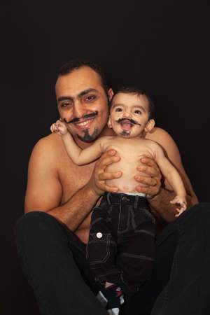 Portrait of a father with a baby with a painted mustache on a black background. High quality photoの写真素材