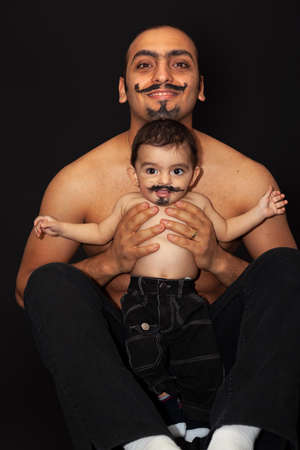 Portrait of a father with a baby with a painted mustache on a black background. High quality photoの写真素材