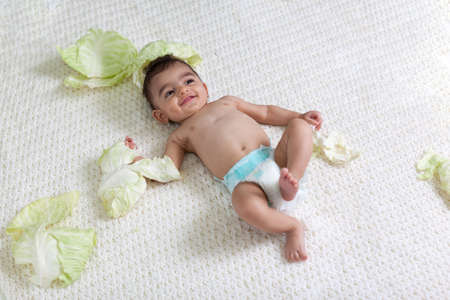 Portrait of a baby in a diaper on a white knitted plaid surrounded by cabbage leaves. High quality photoの写真素材