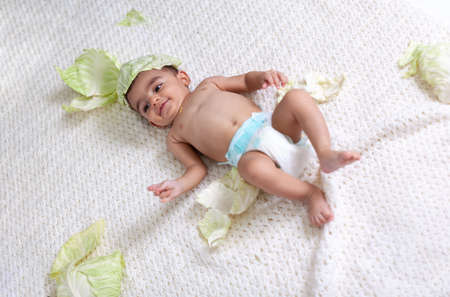 Portrait of a baby in a diaper on a white knitted plaid surrounded by cabbage leaves. High quality photoの写真素材