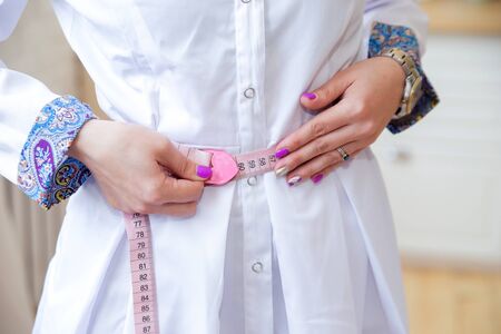 The hands of a slim woman in white medical clothes measure the waistの写真素材
