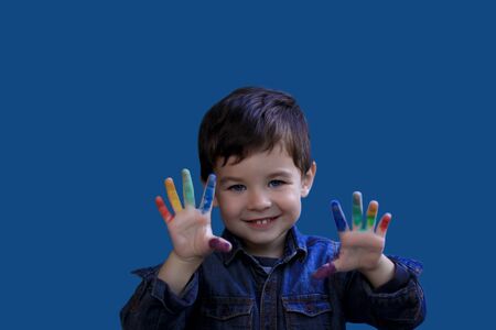 Cute little brunette boy shows fingers stained in colorful paint.の写真素材