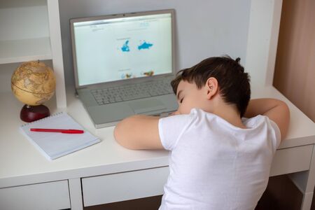 A schoolboy fell asleep behind a monitor from a laptop, holding his head in his hands.の写真素材