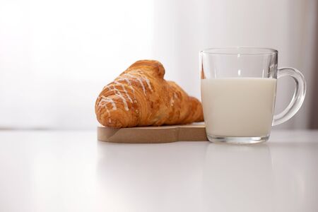 Croissant and glass mug with milk stand on a white tableの写真素材